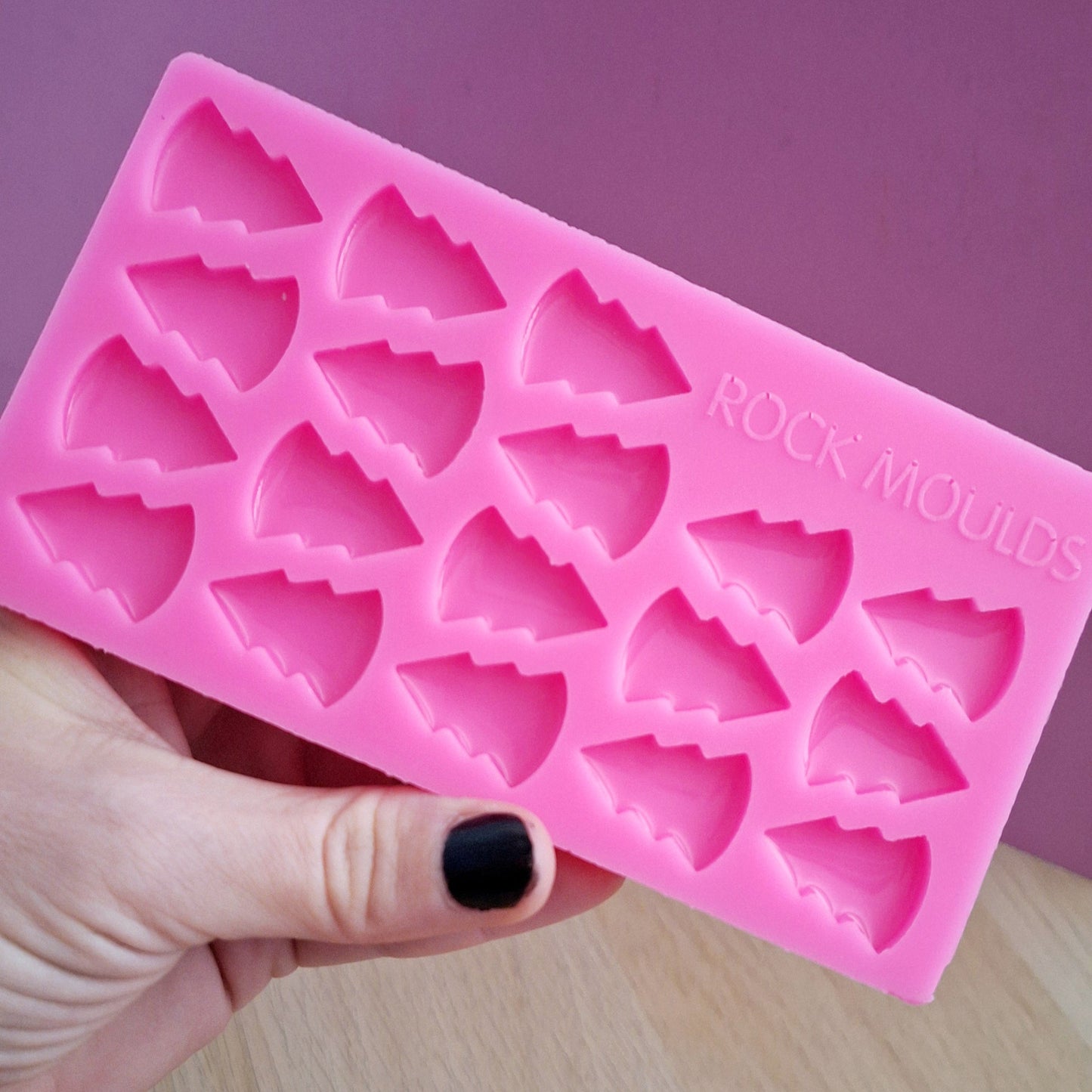 A pink silicone mould in the shape of festive tree studs, held in a person's hand.